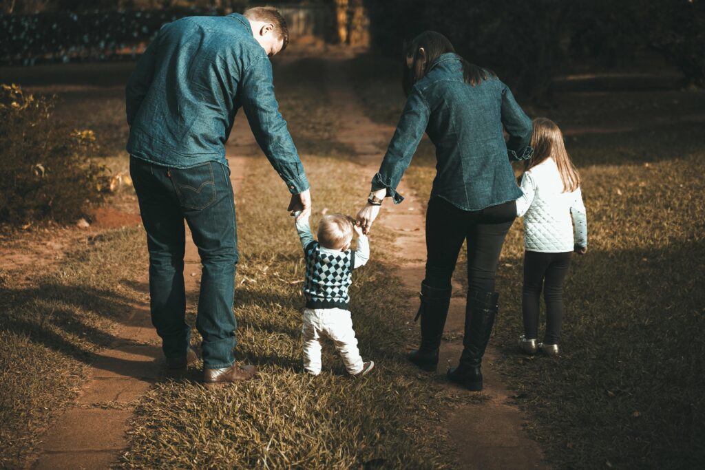 pexels photo 1682497 1682497 A family of four walks hand in hand on a path, enjoying a sunny day outdoors.